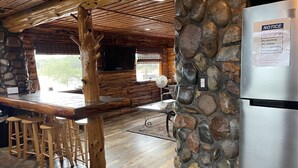 A rustic kitchen with a stone column, wooden bar stools, and a stainless steel refrigerator.