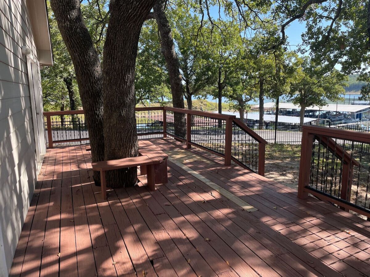 A wooden deck with a bench, surrounded by trees and a railing overlooking a body of water.