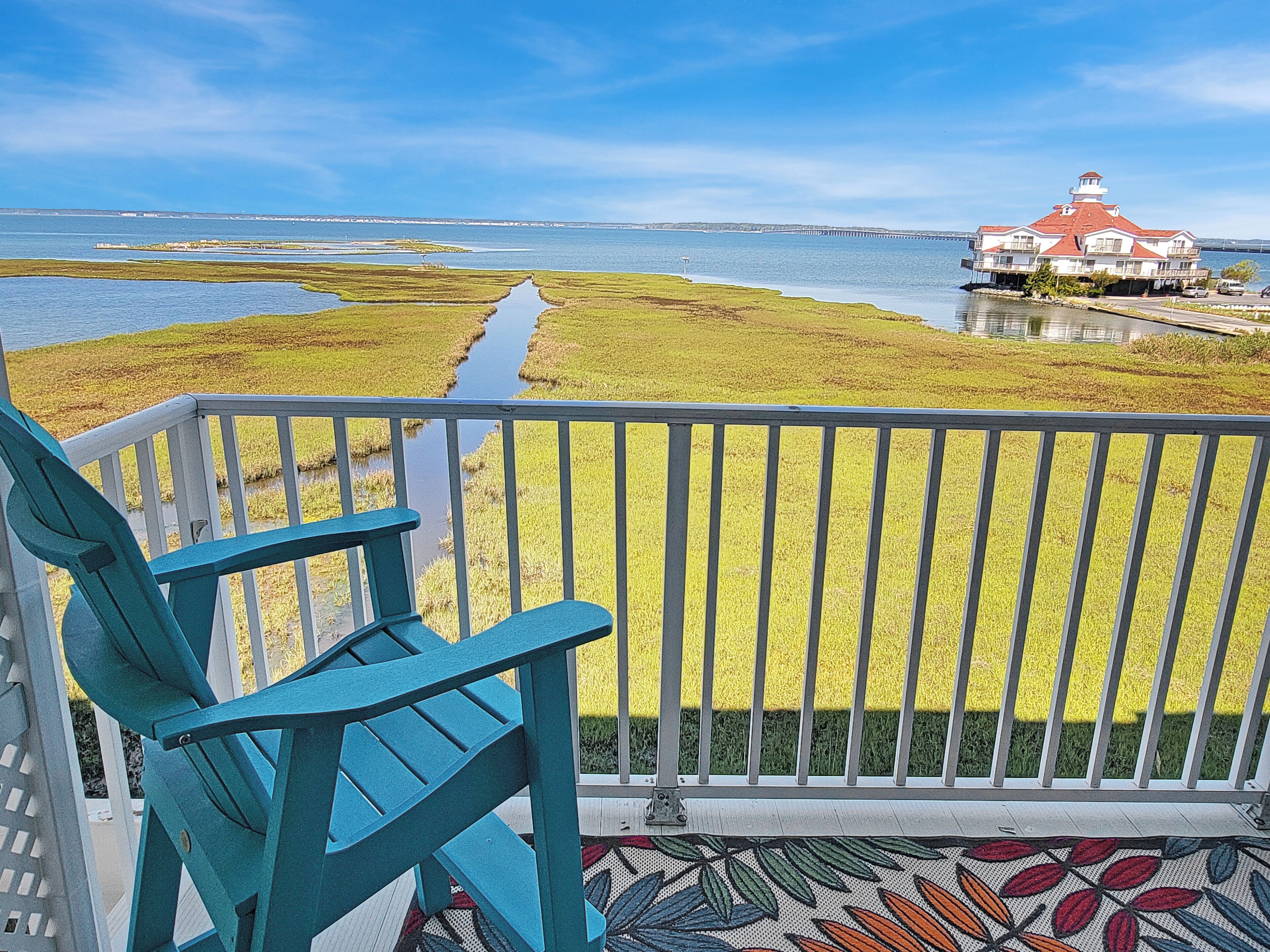 A balcony with a view of a water body and a distant red-roofed building.