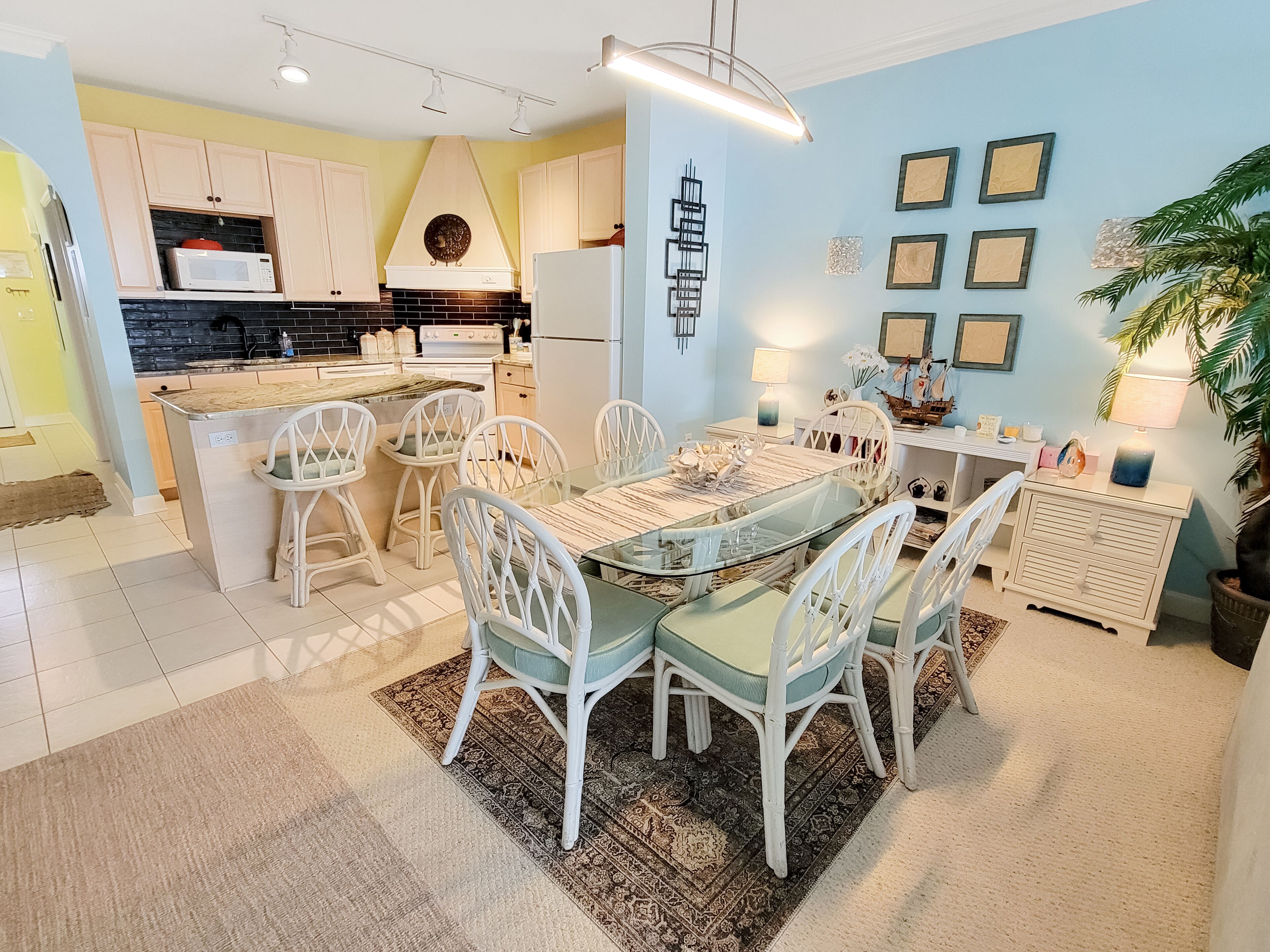 A modern kitchen with white cabinets, a black countertop, and a dining area with a glass table and white chairs.