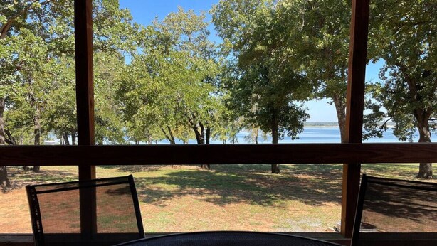 Vista desde una ventana sobre un área con césped, árboles y una masa de agua.