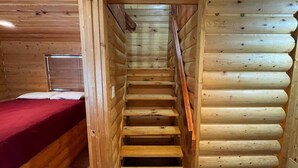 Una escalera de madera que lleva a un dormitorio con una colcha roja.