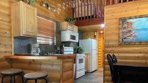 Una cocina de estilo cabaña de madera, con barra, mesa de comedor y un cuadro en la pared.
