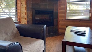 Una habitación acogedora con chimenea, un sofá de cuero y una mesa con controles remotos.