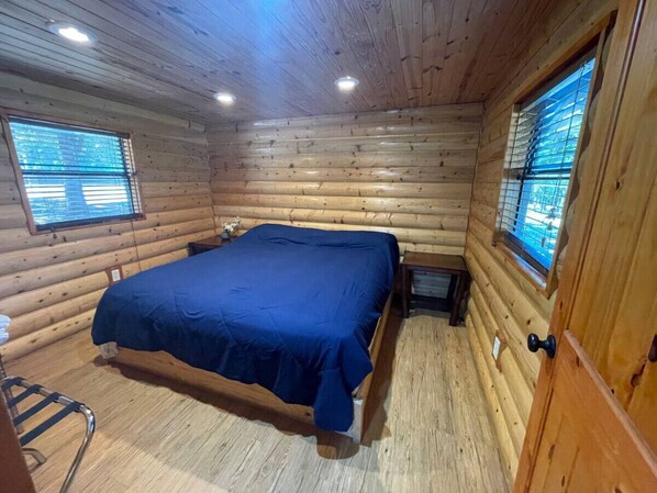 Ein Schlafzimmer in einer Blockhütte mit einem Bett, zwei Fenstern und einer Holztür.