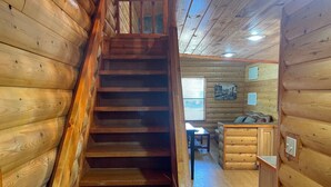 Una escalera de madera conduce a un dormitorio en un altillo con escritorio y cama.