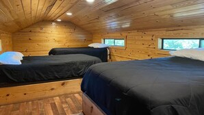 Een blokhut met twee bedden, houten wanden en een schuin dak.