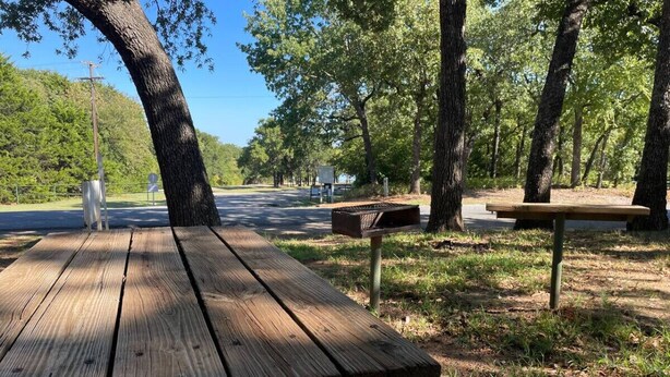 A picnic table in a park with a dirt ground and trees in the background.