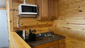 A compact kitchen with wooden cabinetry, a built-in microwave, granite countertop, and a sink.
