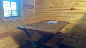 A wooden interior with a table and benches, a window with blinds, and a door.