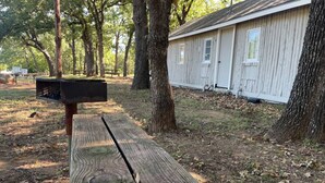A wooden bench in a wooded area with a small building in the background.