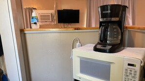 A kitchenette with a microwave oven, a coffee maker, and a small trash bin.