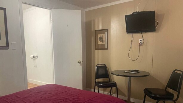 Un dormitorio con una cama, televisión montada en la pared, una mesita y dos sillas.