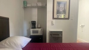 Habitación de hotel con cama, microondas, cafetera y un cuadro en la pared.