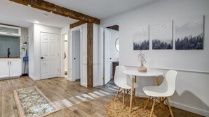 Eine moderne Küche mit weißen Schränken, einem Holzbalken an der Decke und einem Essbereich mit weißen Stühlen und einem runden Tisch.