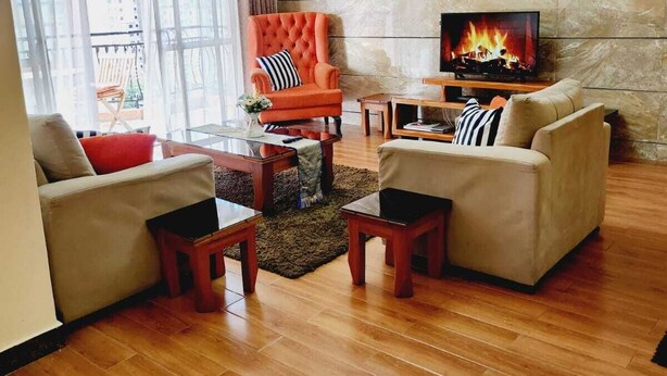 A modern living room with a fireplace, two sofas, a red armchair, and a TV. - Lux Suites Stunning Homes Kilimani (Nairobi)