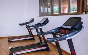Three stationary bikes in a room with wooden flooring and a window with blinds. - Lux Suites Stunning Homes Kilimani (Nairobi)