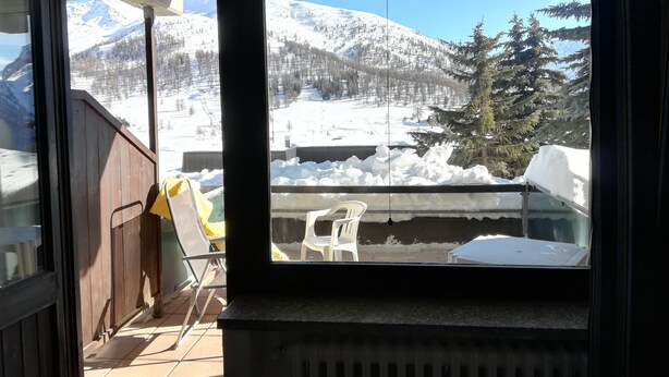 A room with a view of snow-covered mountains and a wooden deck outside. - Sestriere apartment in residence with veranda (Sestriere)