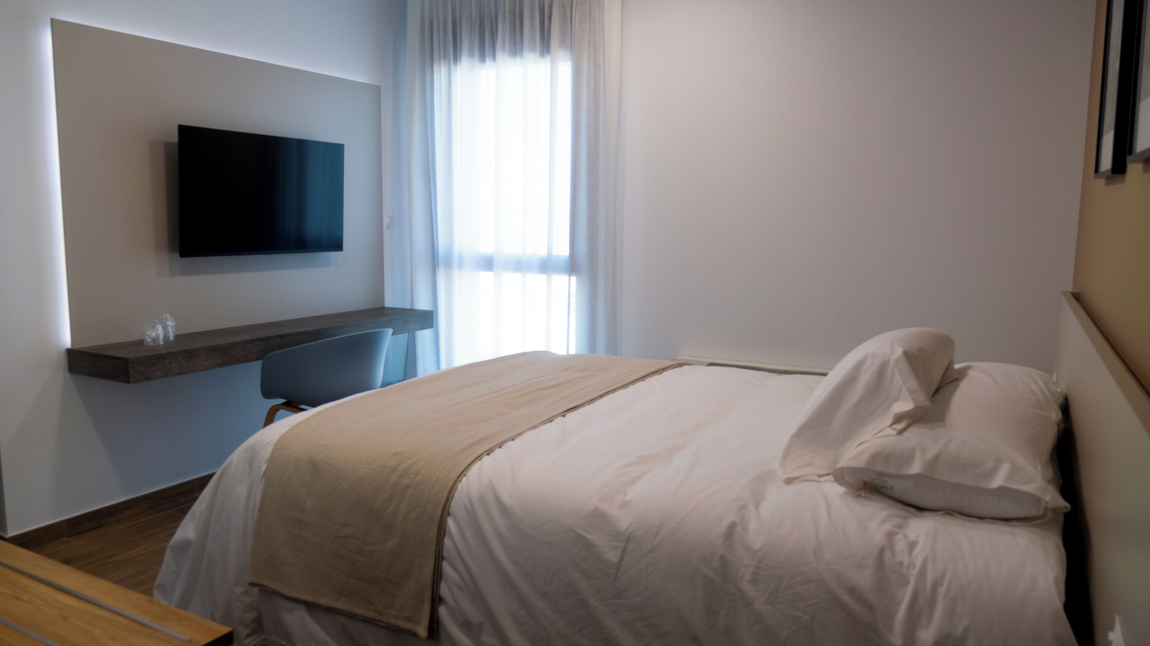 Une chambre d’hôtel avec un lit, un téléviseur fixé au mur, un bureau et une fenêtre avec des rideaux.