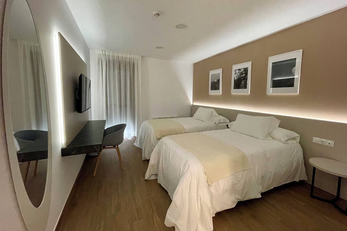 Ein Hotelzimmer mit zwei Betten, einem Schreibtisch, einem Stuhl, einem Spiegel und einem kleinen Tisch.
