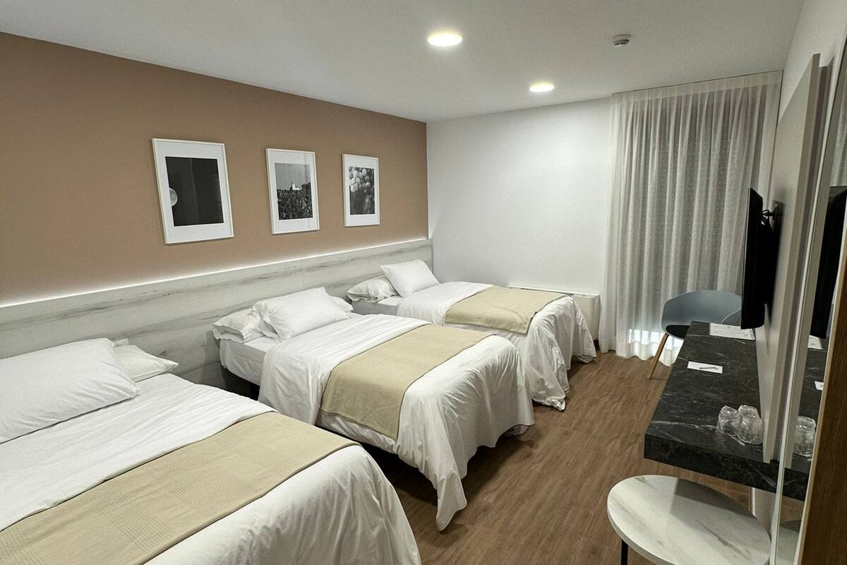 Ein Hotelzimmer mit drei Betten, einem kleinen Schreibtisch, einem Spiegel und einem Fernseher.