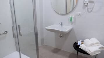 A bathroom with a glass shower enclosure, a sink with a mirror above it, and a small table with towels.