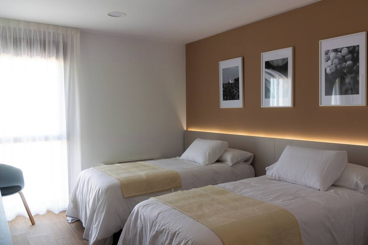 Ein Hotelzimmer mit zwei Betten, einem Sessel und einem kleinen Tisch. An der Wand hängen drei gerahmte Bilder.