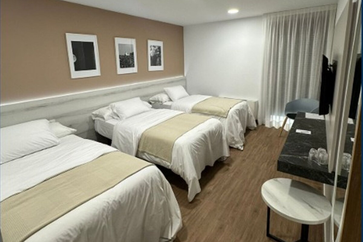 A hotel room with three beds, a small table, and a TV.