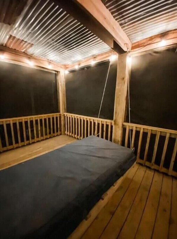 Cozy cabin with a sloped ceiling and wooden beams, featuring a simple bed and a small enclosed area with a wooden railing.