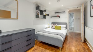 Ein Schlafzimmer mit Bett, Nachttischen, Kommode, Spiegel, Regalen und einer Tür zum Badezimmer.