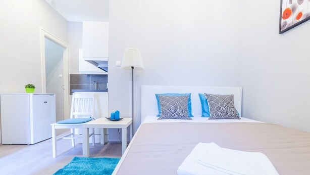 Une chambre d’hôtel comprenant un lit, un bureau, une chaise, une petite table, une lampe et donnant sur la cuisine.