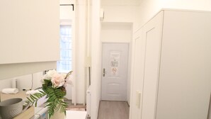 Un couloir étroit, avec une porte blanche au fond, un radiateur et une petite plante posée sur une table.