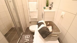 Une salle de bain avec douche, toilettes et un petit lit avec un tapis.