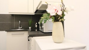 Une cuisine moderne avec des meubles blancs, un plan de travail noir, un évier en acier inoxydable, une machine à café et un vase rempli de fleurs.