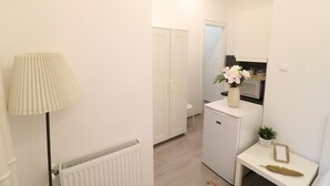 Une petite pièce propre, avec un radiateur, une armoire blanche, une petite table sur laquelle est posé un vase de fleurs et un meuble blanc.