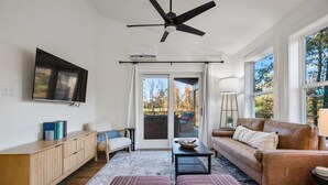 Un saló modern amb un sofà, otomans, una taula de centre i un televisor fixat a la paret.