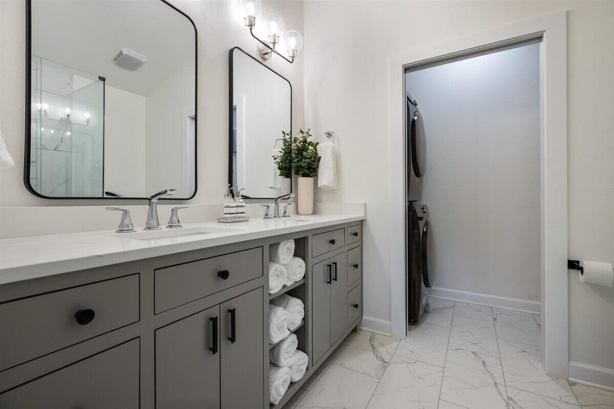 Une salle de bain moderne avec un grand miroir, deux lavabos, un porte-serviettes et un espace douche.