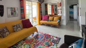 A spacious living area with a yellow sofa, colorful rug, and a dining table.