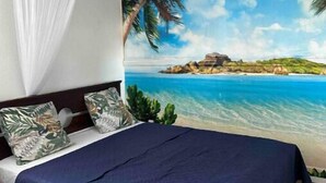 A bedroom with a bed, a ceiling fan, a large beach mural, and a night sky.