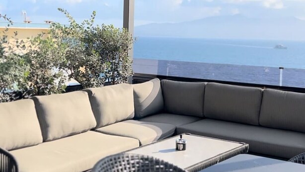 Un área de estar moderna al aire libre con un sofá y una mesa, con vista a un paisaje marino.