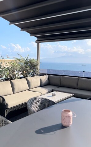 Un área de estar moderna al aire libre con un sofá y una mesa, con vista a un paisaje marino.
