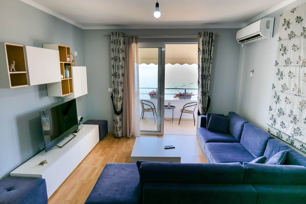 A modern living room with a flat-screen TV, a sofa, a coffee table, and a balcony with a view.