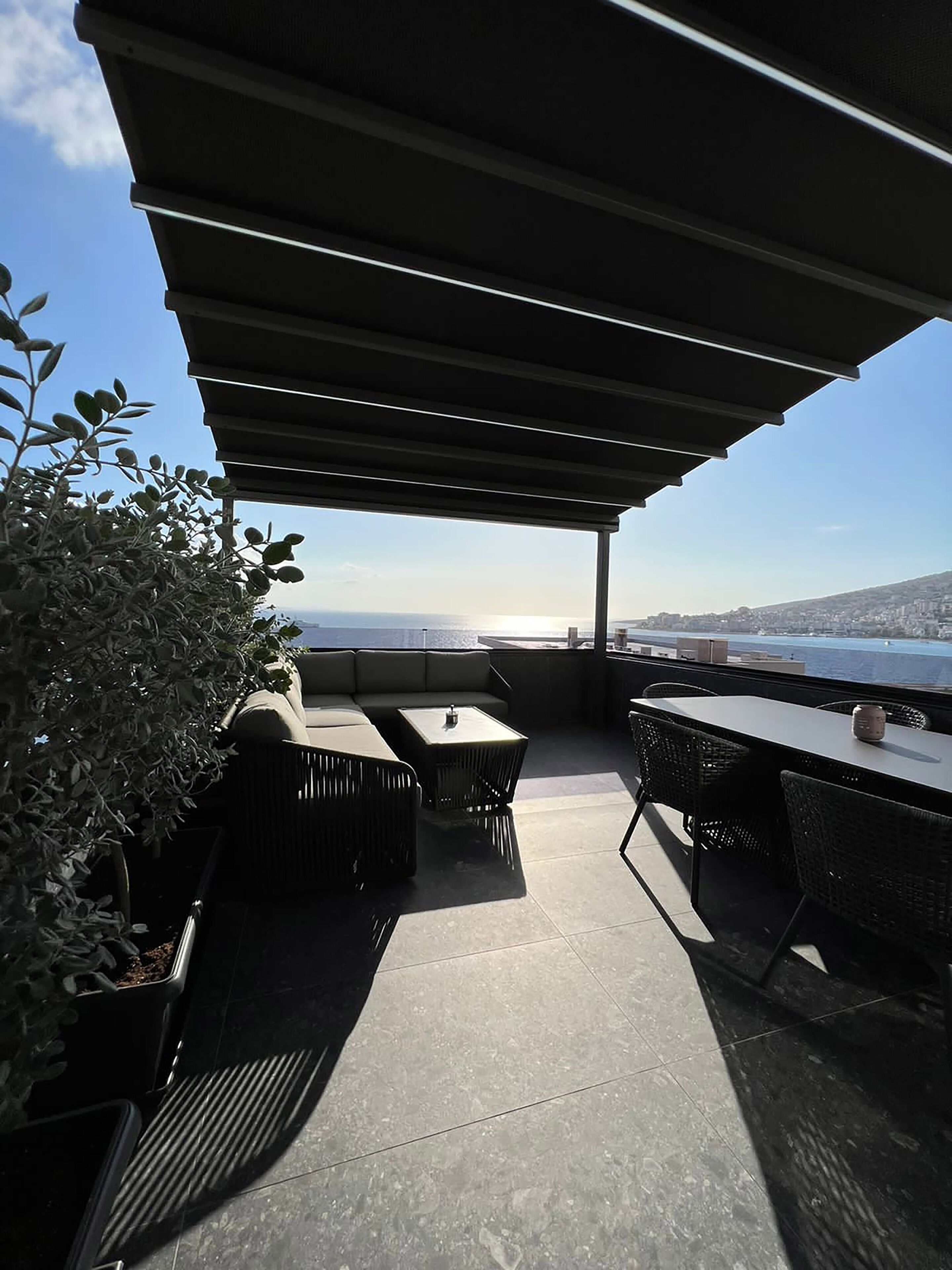 An outdoor patio with a covered seating area, a table, and potted plants.