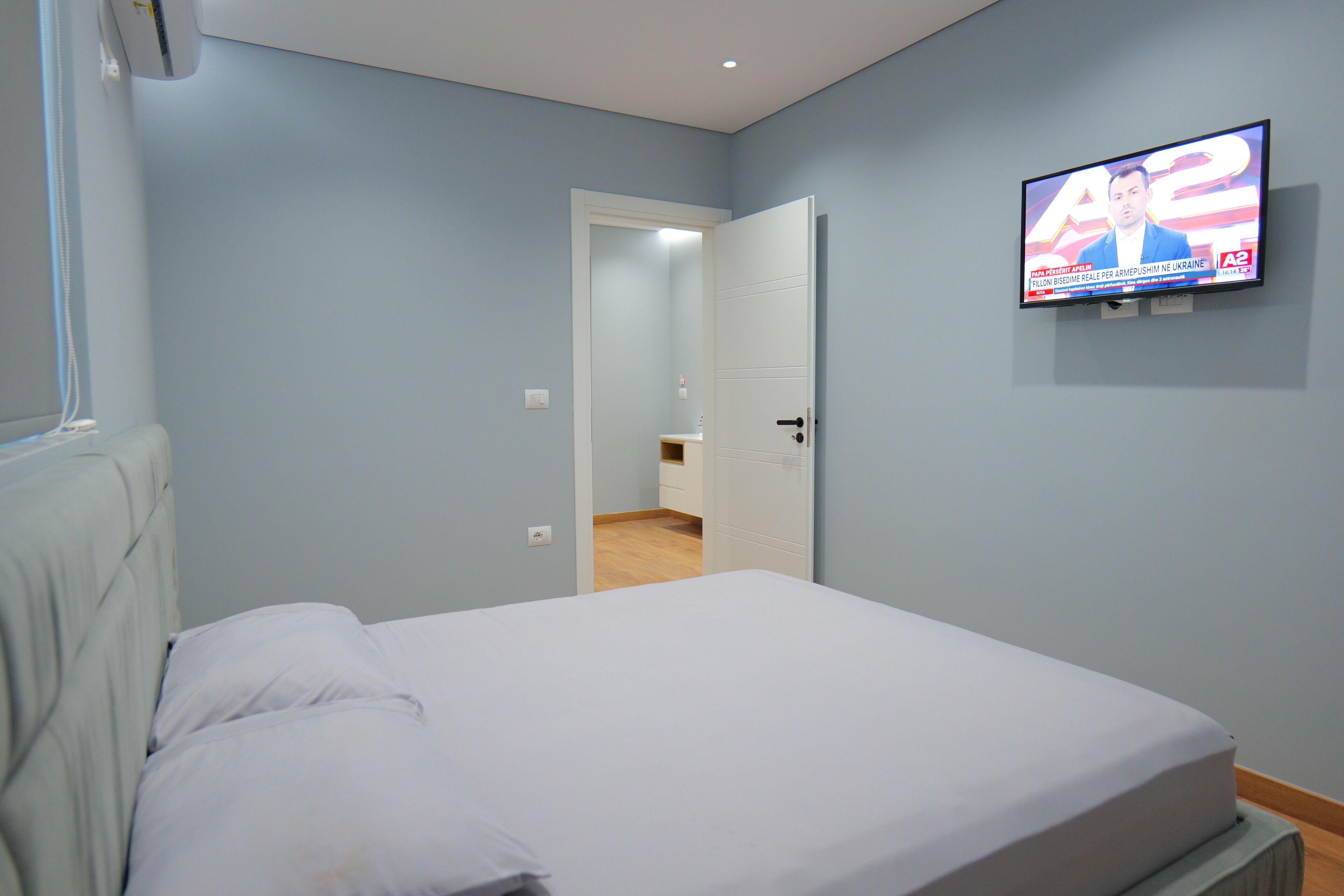A bedroom with a bed, a television mounted on the wall, and a door leading to another room.
