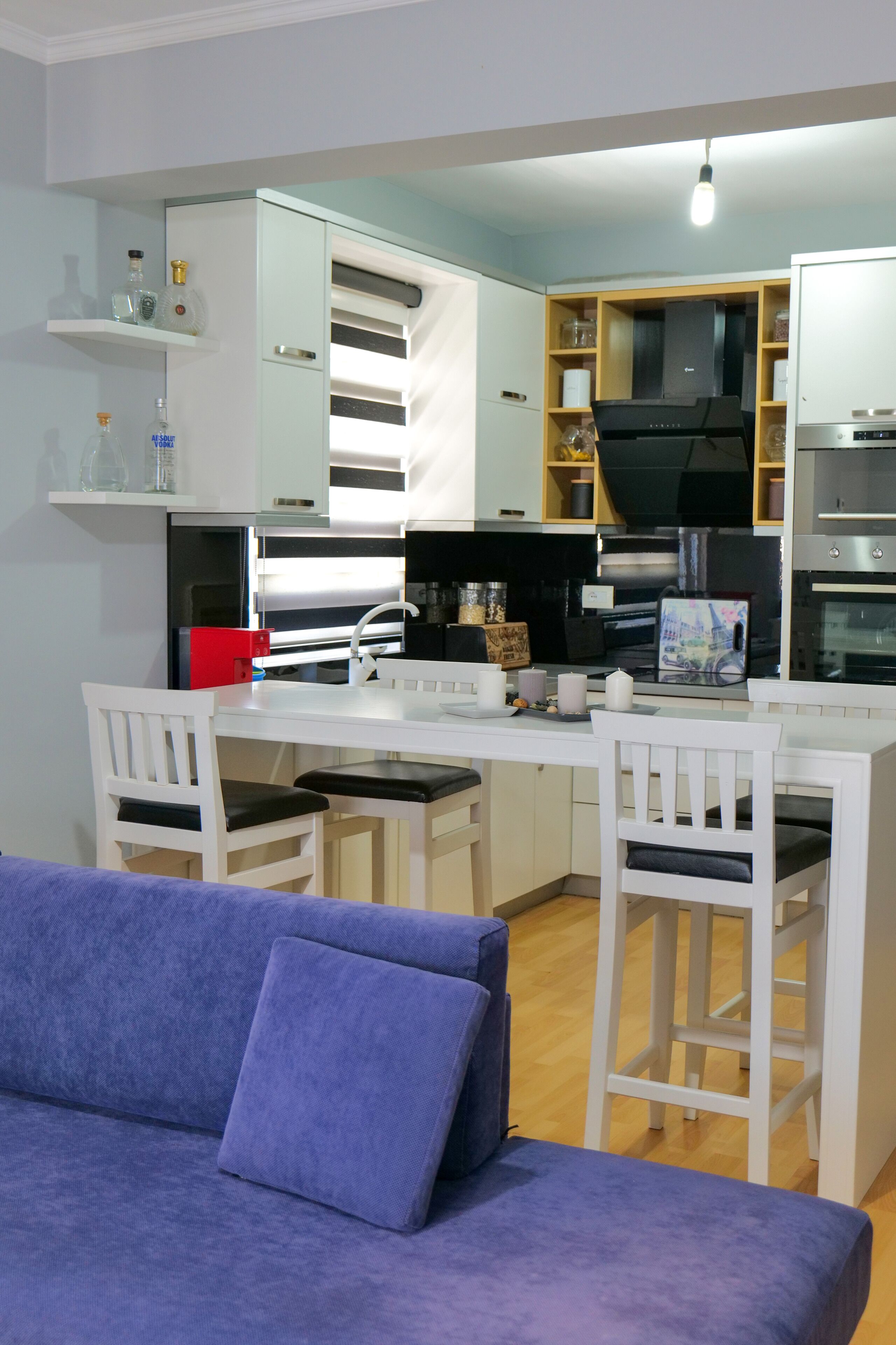 Una cocina compacta con armarios blancos, una estufa negra y una pequeña zona de comedor con sillas blancas.