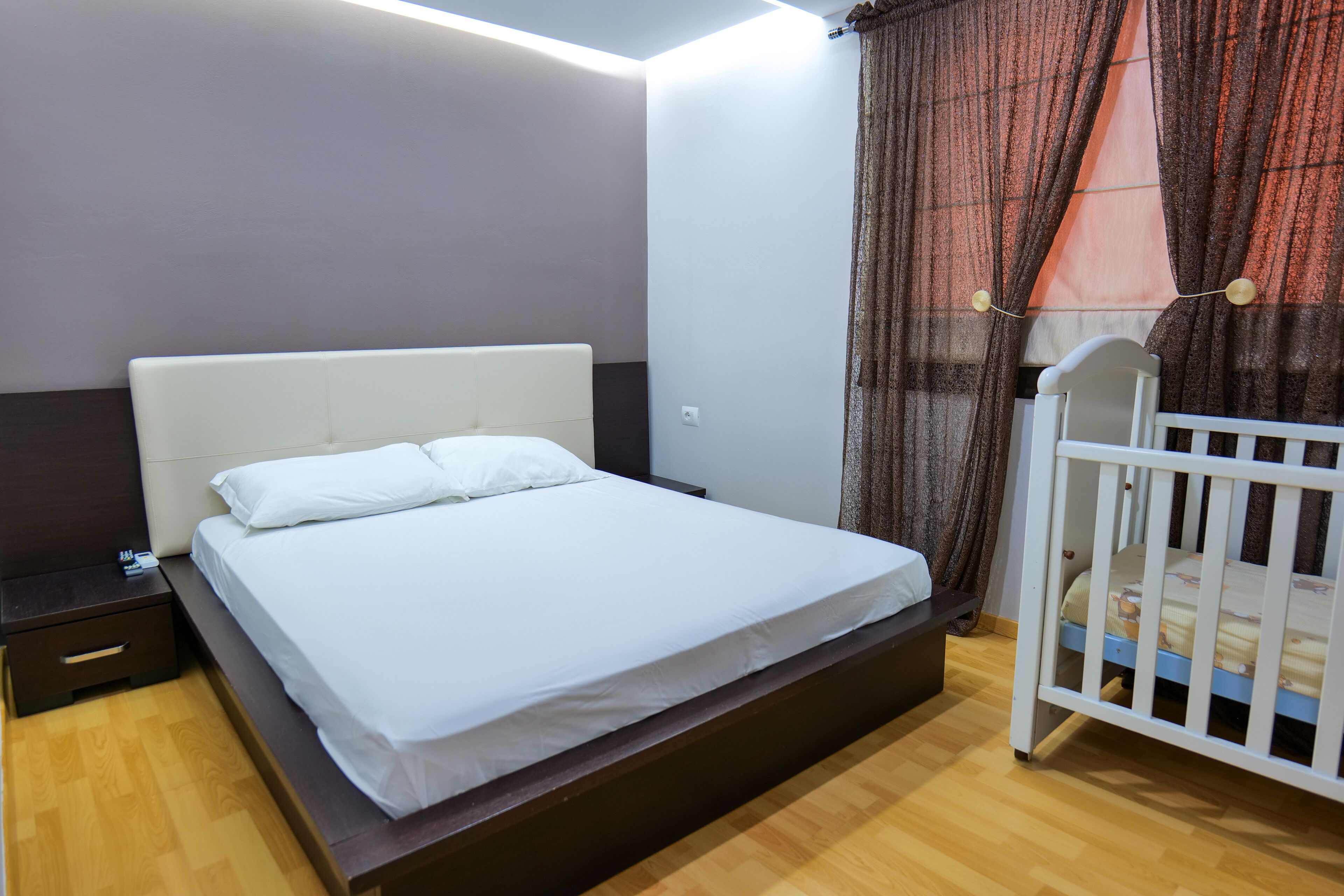 Une chambre à coucher avec un lit, une table de chevet, un berceau et un rideau.