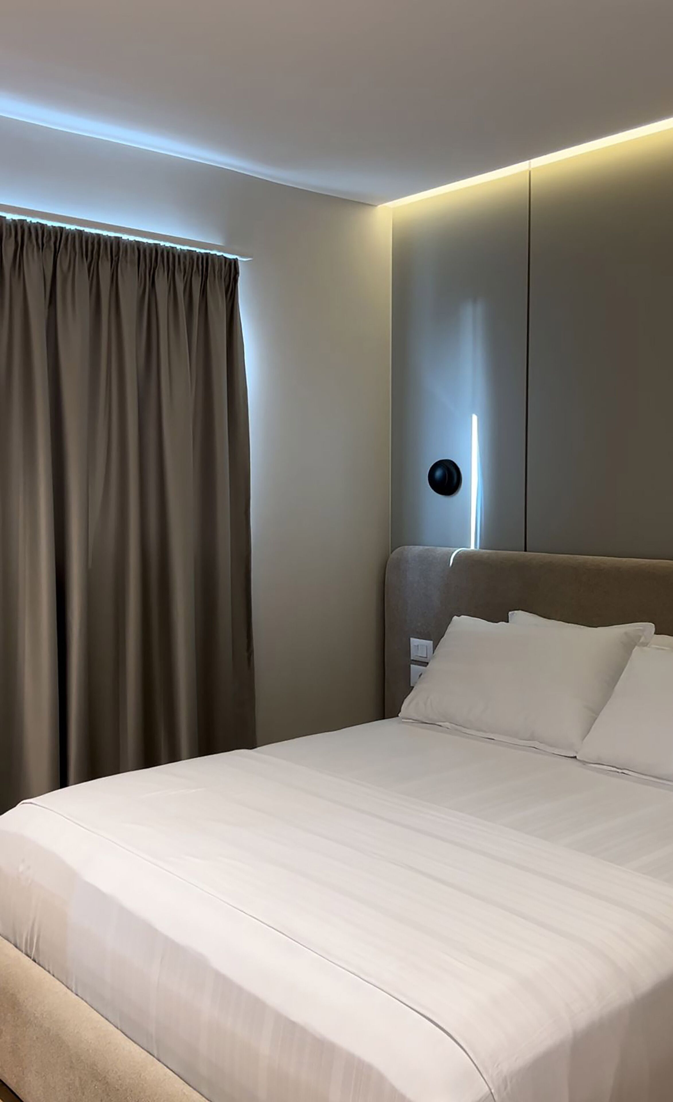 A hotel room with a large bed, a headboard with a light fixture, and a curtain.