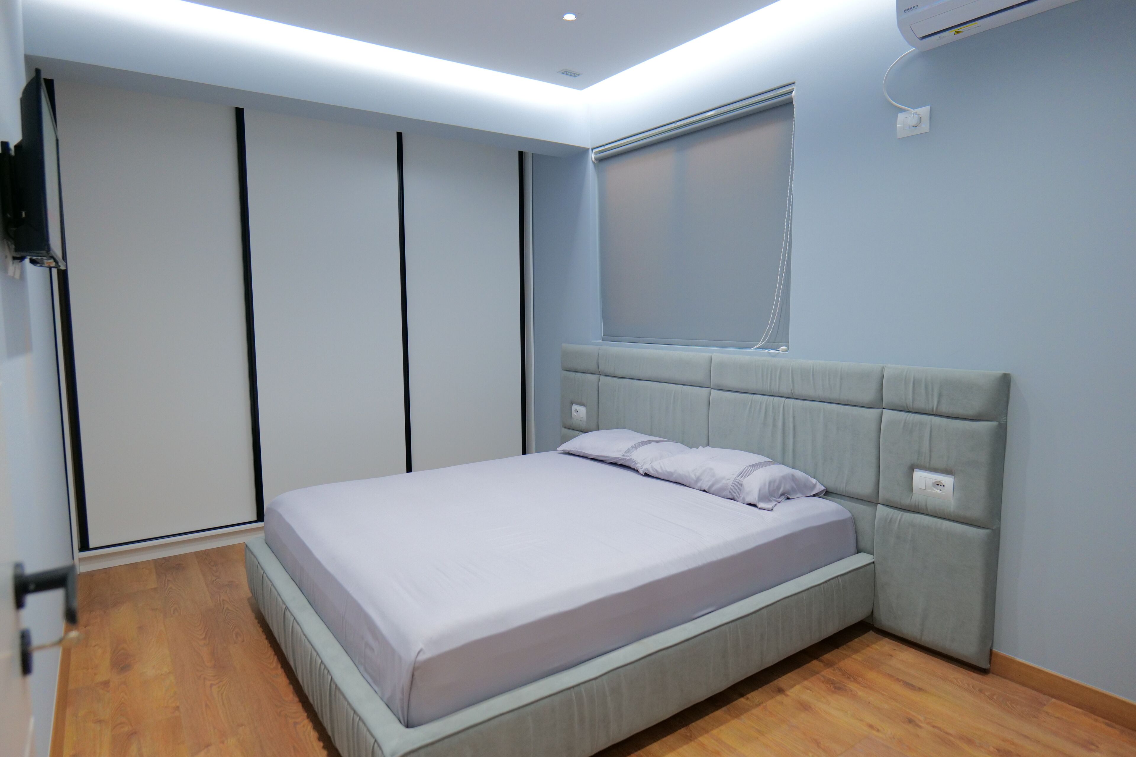 A modern bedroom with a bed, wooden flooring, a built-in wardrobe, and a window with blinds.