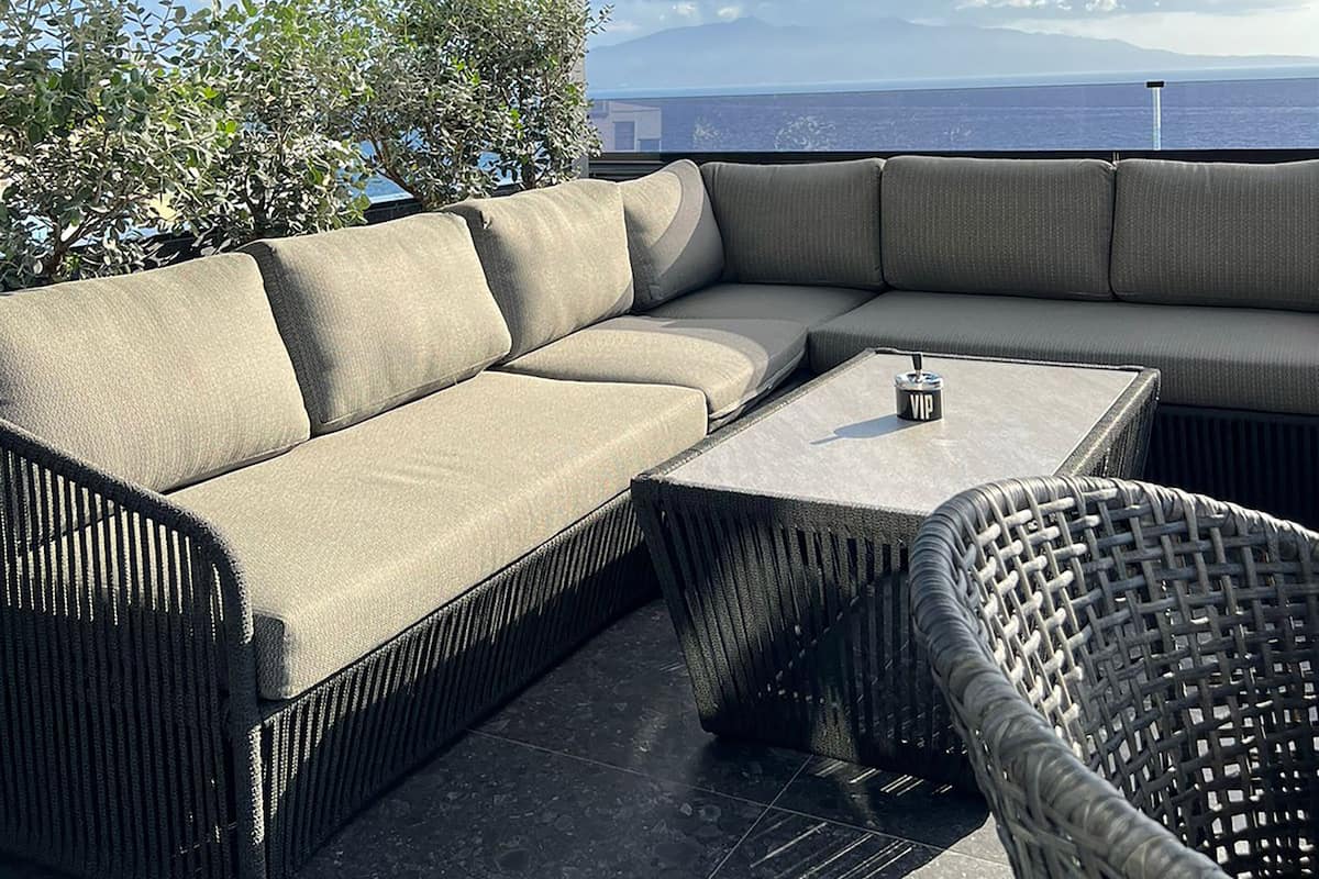 A covered outdoor seating area with a sofa and a table, overlooking a scenic view.