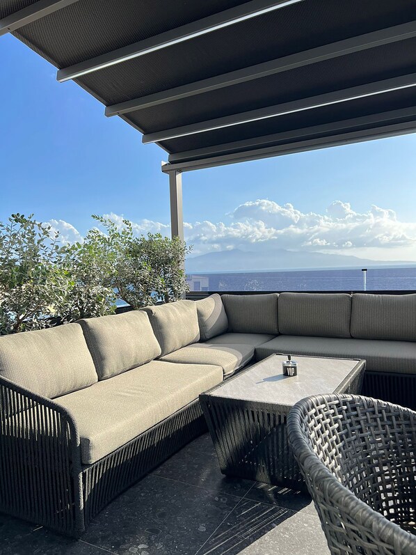 A covered outdoor seating area with a sofa and a table, overlooking a scenic view.